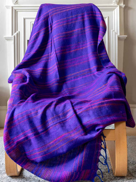 Purple plaid blanket draped over a wooden chair against a white wall.