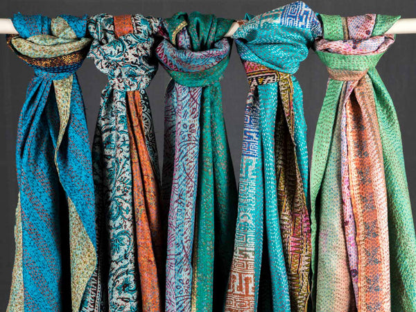 Colorful patterned scarves hanging on a rod against a dark background