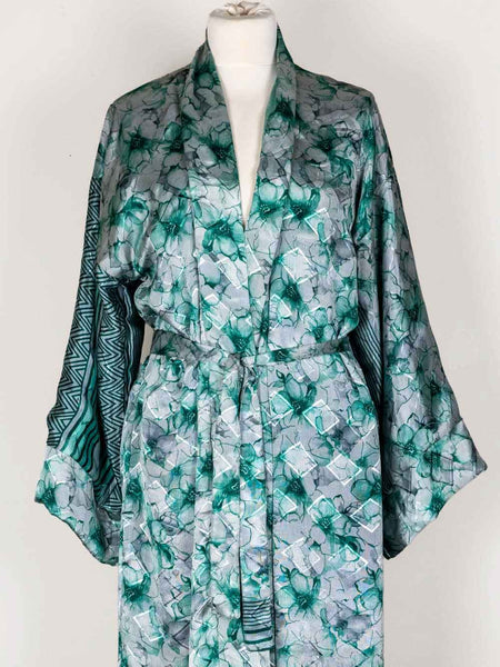A long-sleeved kimono-style robe displayed on a white mannequin torso against a plain light background. The robe features a watercolor-style green and gray floral pattern with a matching tie belt and a contrasting dark green geometric pattern on the sleeves.