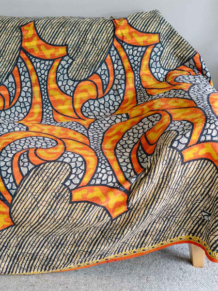 Textile with orange, gray, and black abstract pattern draped over a chair.