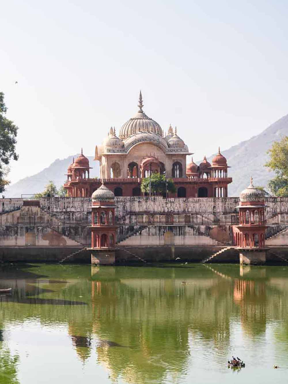 Traditional temple with a dome and arches reflected in a pond with mountains in the background