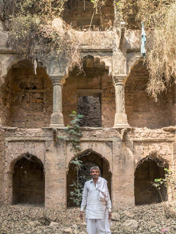 Man standing in front of an old, dilapidated architectural structure with arched entrances.