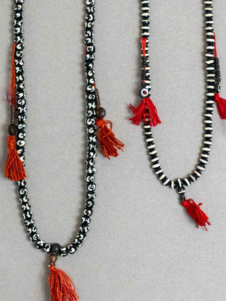 Two beaded necklaces with red tassels on a light gray background