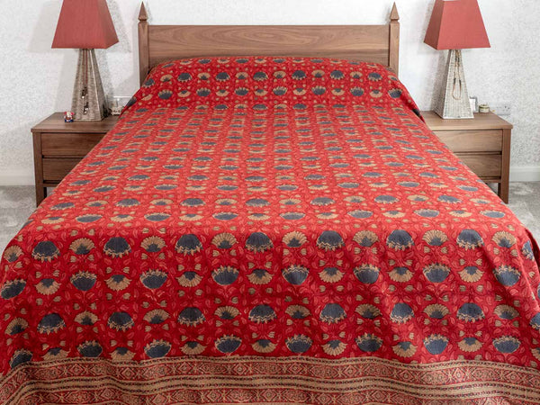 Red patterned bedspread on a wooden bed with matching nightstands and lamps.