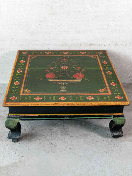 Decorative wooden table with green paint and floral patterns on a plain background
