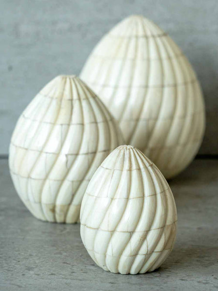 Three white textured egg-shaped sculptures on a gray surface