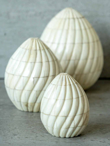 Three white textured egg-shaped sculptures on a gray surface