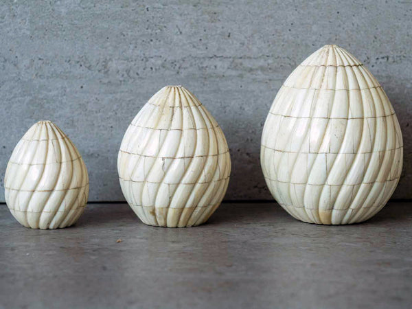 Three decorative egg-shaped objects with textured surfaces on a concrete surface.
