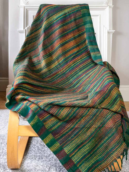 Striped green blanket draped over a wooden chair against a white wall.