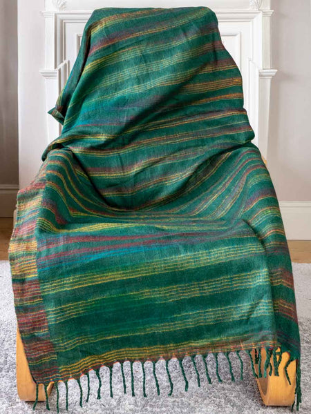 Green plaid blanket draped over a wooden chair against a white wall.