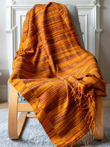 Orange striped blanket draped over a wooden chair in a room with white walls.