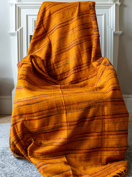 Gold striped blanket draped over a chair in a room with white walls.