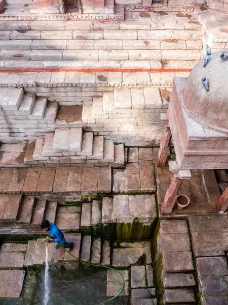 Person cleaning a stepwell with water, surrounded by stone steps and walls.