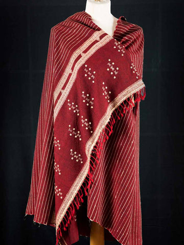 Red shawl with white patterns and fringes on a mannequin against a black background