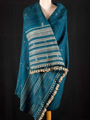 Blue shawl with white patterns draped over a mannequin against a black background