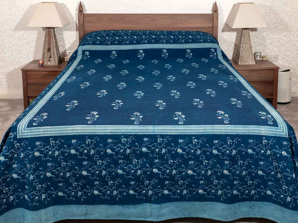 Blue floral-patterned bedspread on a bed with wooden nightstands and lamps in a room.