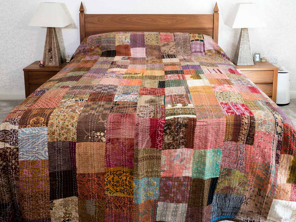 Multicolored bronze patchwork bedspread on a bed in a bedroom setting.