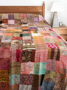 Multicolored bronze patchwork bedspread on a bed in a bedroom setting.