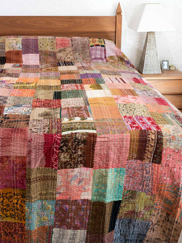 Multicolored bronze patchwork bedspread on a bed in a bedroom setting.
