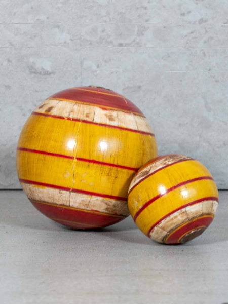 Two wooden balls with red and beige stripes on a gray surface.