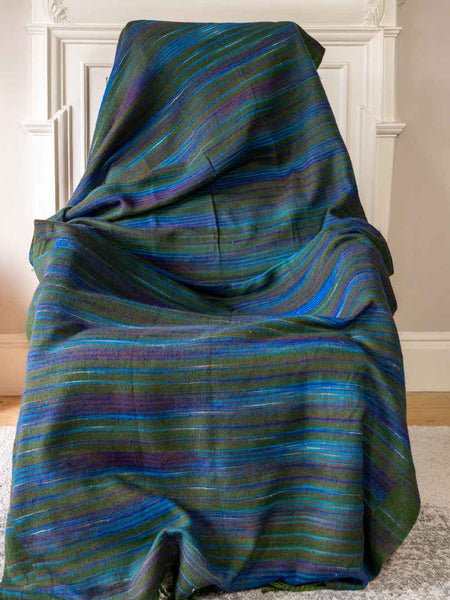 Blue and green striped blanket draped over a chair against a white wall.