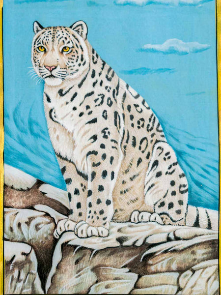A painted artwork of a snow leopard seated on rocks against a bright blue sky, with a yellow border around the artwork.