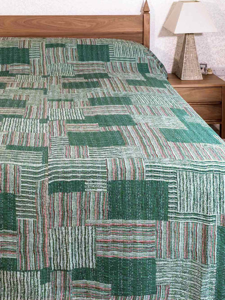 Green patterned quilt on a bed with a wooden headboard and nightstand.