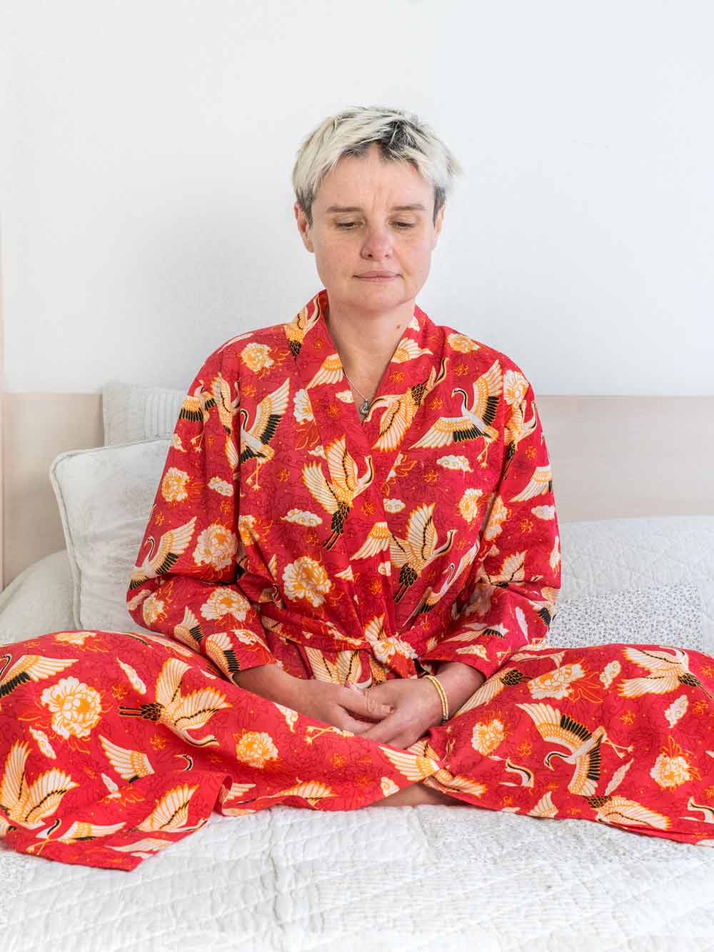 Person wearing a red floral kimono sitting on a bed.
