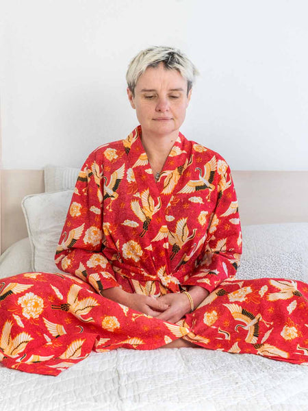 Person wearing a red floral kimono sitting on a bed.