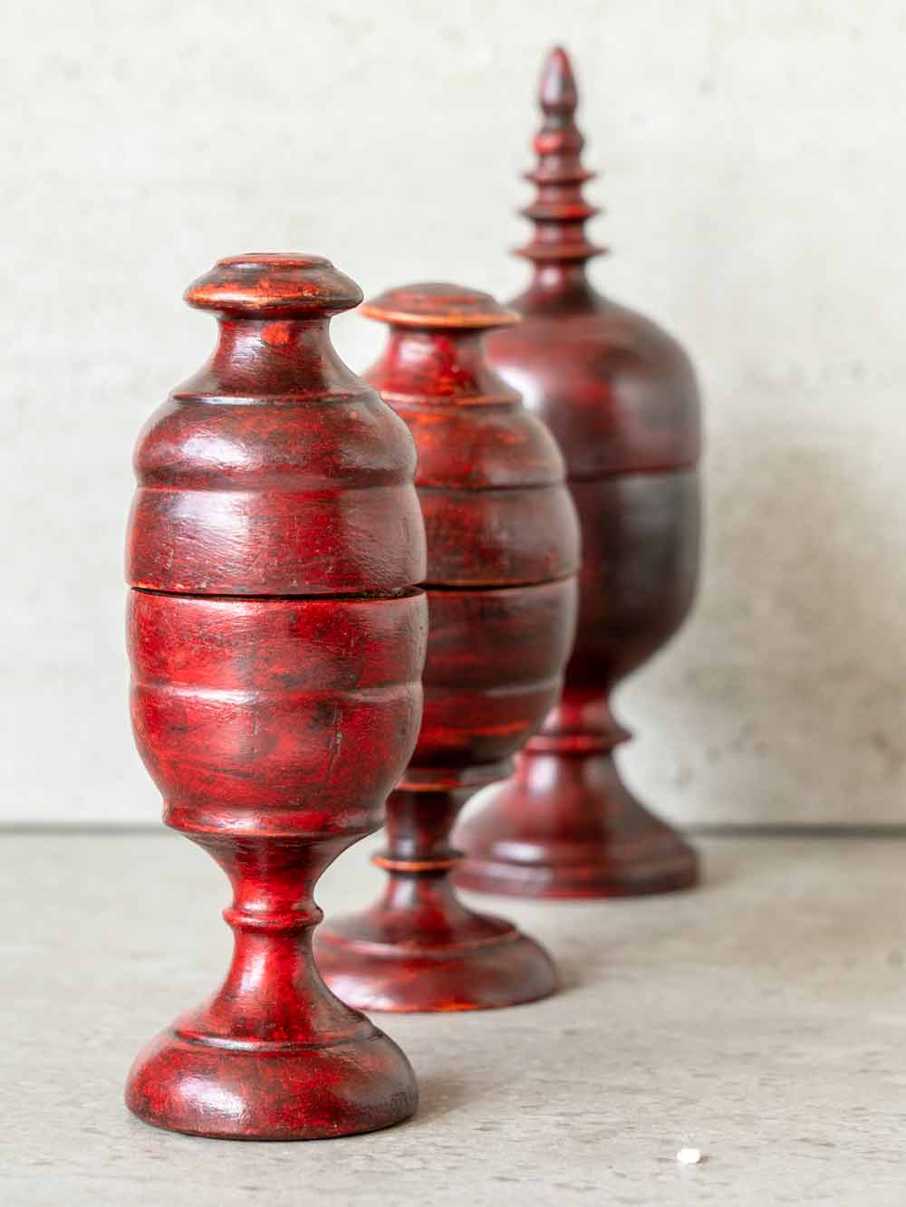 Three red wooden tkka boxes of varying sizes on a light surface with a neutral background