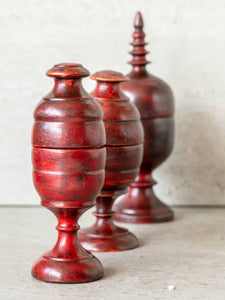 Three red wooden tkka boxes of varying sizes on a light surface with a neutral background