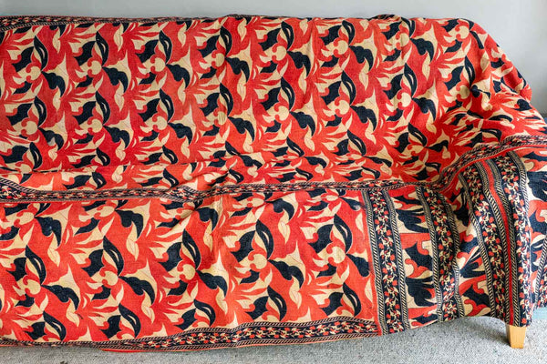 Sofa with a vibrant red, black, and beige patterned cover against a neutral background
