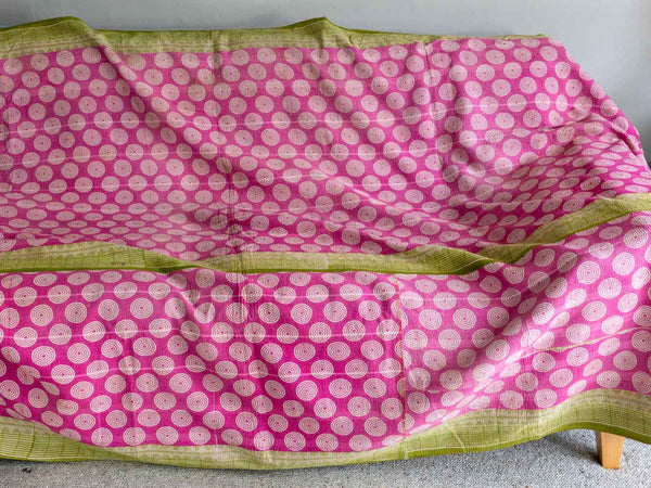 Pink saree with white circular patterns and green border on a gray background