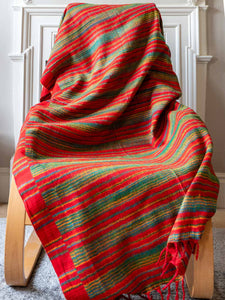 Colorful striped blanket draped over a wooden chair against a white wall.
