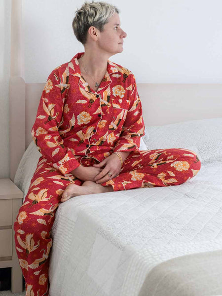 Person wearing red floral pajamas sitting on a bed.