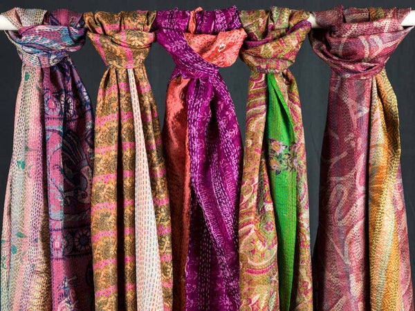 Five pink & red patterned scarves hanging side by side against a dark background