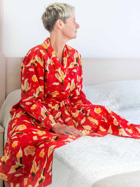 Person wearing a red kimono with gold and black patterns sitting on a bed.