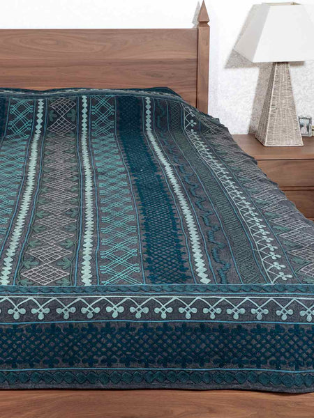 Blue patterned bedspread on a wooden bed with a lamp in the background.
