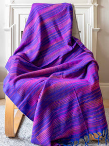Purple and blue striped blanket draped over a chair in a room with white walls.