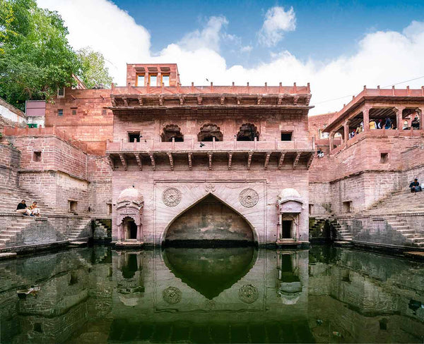 Historic stone structure with arch and water reflection, surrounded by greenery