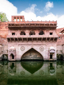 Historic stone structure with archway over water, under a blue sky with clouds.