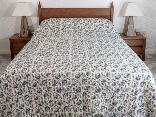 Bed with floral patterned comforter in a bedroom setting with wooden nightstands and lamps.