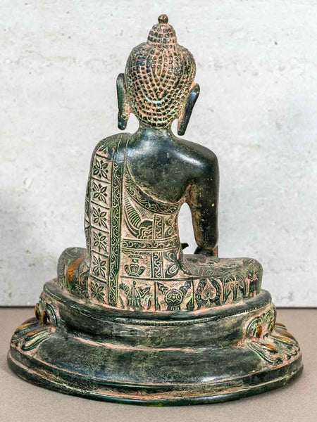 Bronze Buddha statue with intricate designs on a textured white background