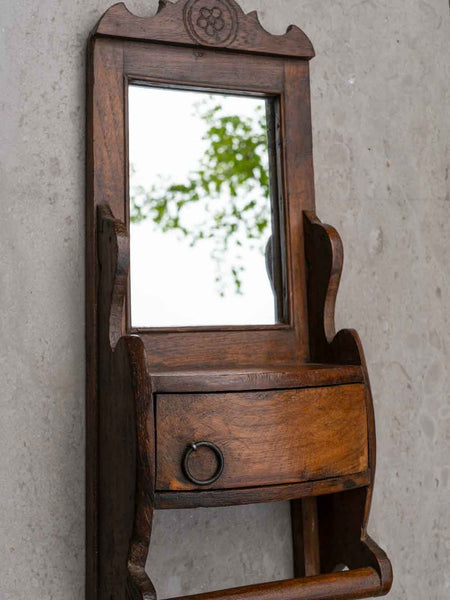 Wooden mirror with a drawer against a textured wall