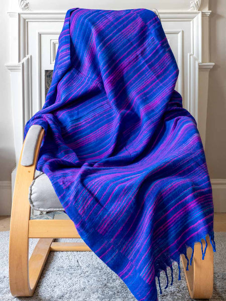 Blue and purple striped blanket draped over a wooden chair in a room with white walls.