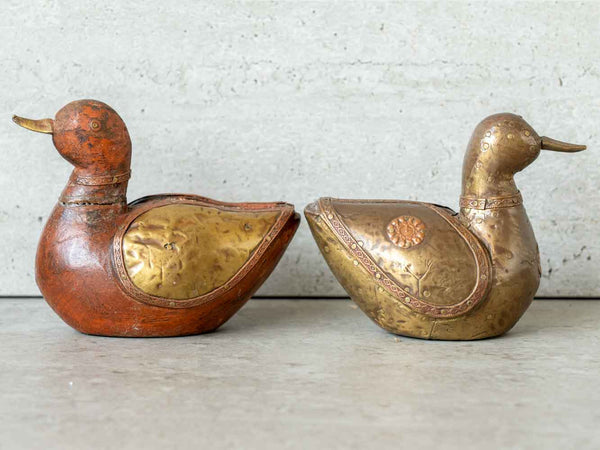 Two decorative duck-shaped items, one wooden and one brass, on a light background.