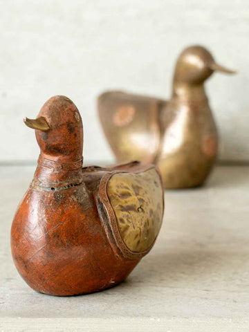 Two vintage-style duck figurines, one wooden and one brass, on a neutral background.