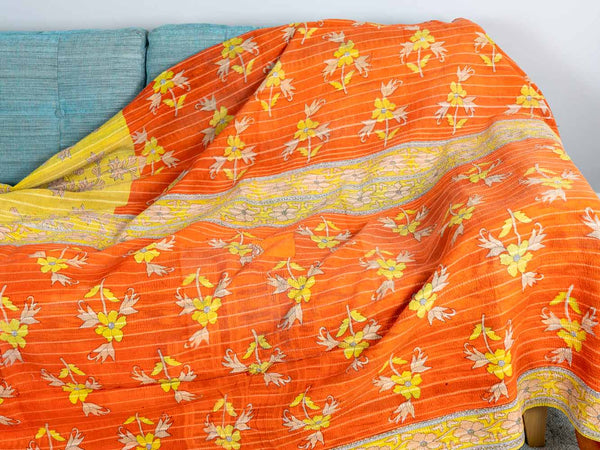 Orange fabric with yellow floral patterns draped over a blue sofa.
