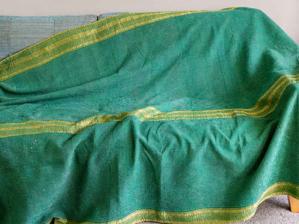 A green woven throw blanket with gold stripes draped over a gray sofa.