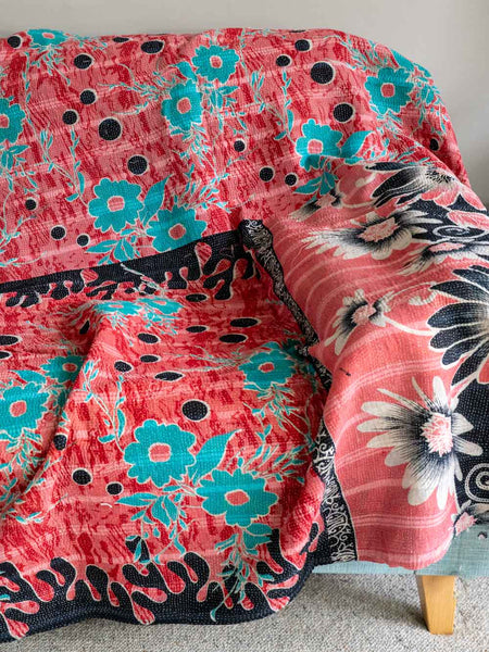 Floral patterned blanket with pink, blue, and black colors draped over a chair.
